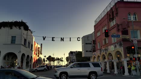 Venice-sign-panning-shot-at-corner-of-Pacific-Ave---Windward-Ave-with-traffic-,-during-sunset,-in-Los-Angeles,-California,-USA