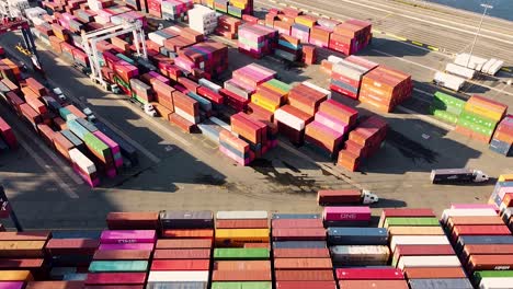 Industrial-vehicles-moving-and-sorting-shipping-containers-at-busy-shipping-port-near-New-York-City---pan-up-aerial-footage