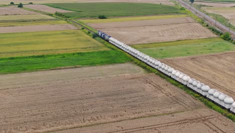 Cargo-train-with-silo-wagons-moves-through-fields-in-rural-Poland-Europe,-aerial
