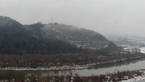 Winterlandschaft-Am-Berghang-Mit-Bergstraße-Und-Friedlichem-Fluss,-Luftaufnahme