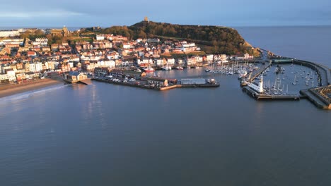 Drone-shot-of-a-town-with-a-hill-and-a-harbor-with-boats-during-daytime-in-Scarborough-North-Yorkshire,-England