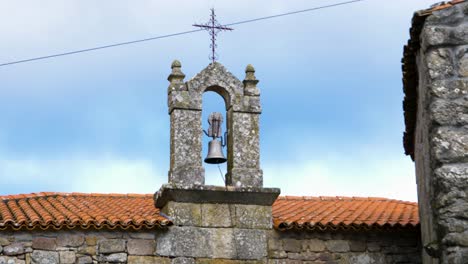 Wide-angle-view-of-iron-bell-resting-between-stone-pillar-arch-on-orange-roof-church