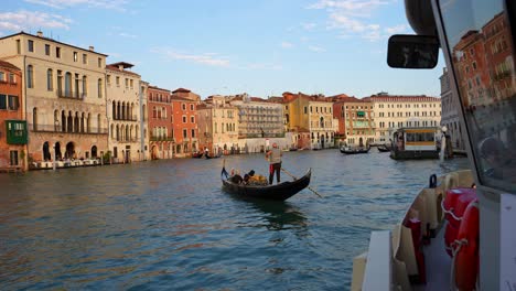 Gondolier-rowing-gondola-on-Grand-Canal-with-tourists-at-sunset-seen-from-a-Vaporetto