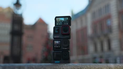 Four-small-tiny-compact-action-cameras-mounted-together-on-tripod-with-defocused-cityscape-in-background