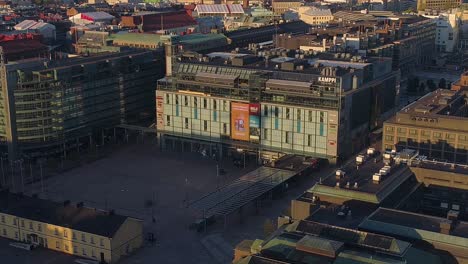 Aerial-view-around-the-Kamppi-shopping-centre,-sunny,-summer-morning-sunrise,-in-Helsinki,-Finland---orbit,-drone-shot