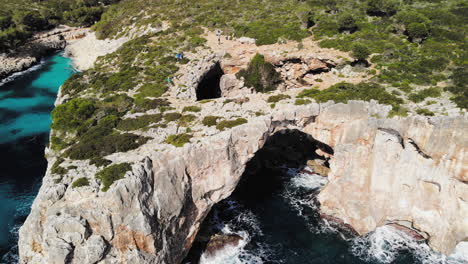 A-forward-flying-drone-shot-towards-a-sea-arch-with-tourists-walking-around-near-Cala-Varques-in-Majorca