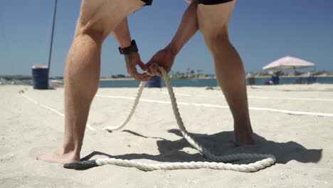 Male-athlete-prepares-to-pull-kettlebells-on-rope-during-beach-fitness-competition---anticipation-
