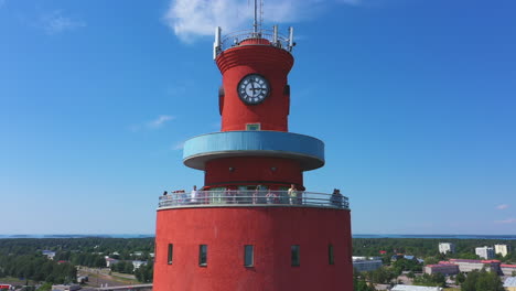 Tourists-Sightseeing-Top-of-Hanko-Water-Tower-Under-Blue-Sky,-Finland,-drone-tilt-down