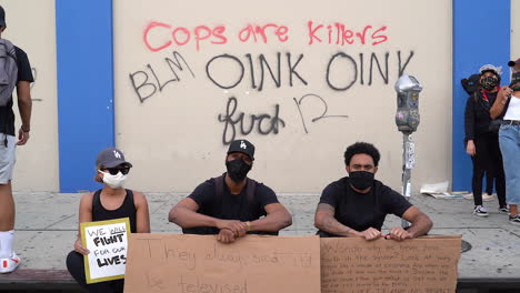 Maskierte-Black-Lives-Matter-Demonstranten-Sitzen-Auf-Dem-Bürgersteig,-Los-Angeles,-Zeitlupe