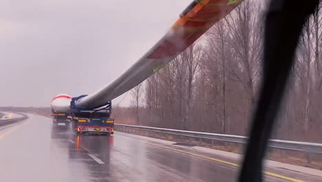 POV-of-a-car-driving-on-the-highway-on-a-rainy-day-with-huge-windmill-fan-passing-on-the-truck