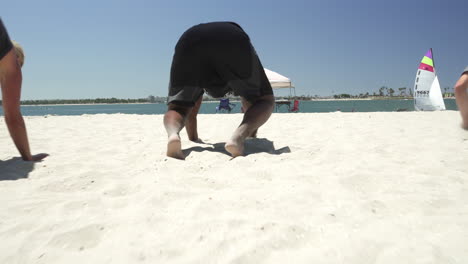 Multiethnic-male-athletes-doing-bear-crawls-during-beach-workout