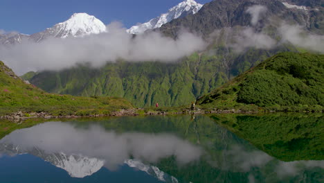 Drone-shot-landscape-Nepal-green-hills-and-mountain-clouds,-girl-walks-wearing-pink-saree,-lake-reflection-4K