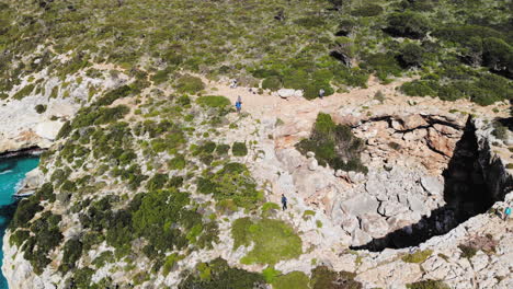 Un-Dron-Volador-Hacia-Atrás-Disparó-Sobre-Un-Arco-Marino-Con-Algunos-Turistas-Caminando-Cerca-De-La-Playa-De-Cala-Varques-En-Mallorca