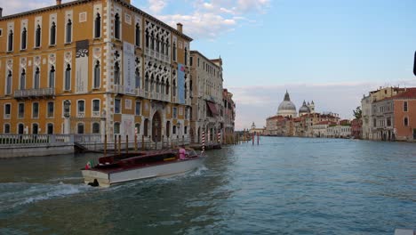 Boat-navigating-Venice-Grand-Canal-surrounded-by-buildings-and-Basilica-in-background,-Italy