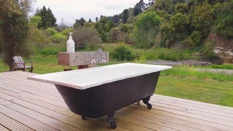 Eine-Badewanne-Mit-Löwenfüßen-Im-Freien-Auf-Einer-Holzterrasse-In-Der-Natur-An-Einem-Fluss-In-Neuseeland
