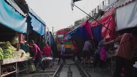 Tracking-Shot,-Vendors-Setting-up-their-Store-in-Maeklong-Samut-Rail-Road-Market,-Thailand,-Train-Passing-Rail-Road-in-the-background