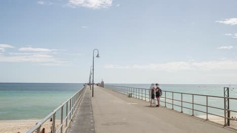 Time-lapse-of-people-walking-along-jetty-at-midday,-slow-zoom-out