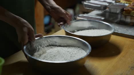 2-bowls-of-plain-flour-being-sifted-by-hand-on-wooden-kitchen-tabletop,-filmed-as-medium-closeup-slow-motion-shot