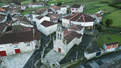 Wide-angle-aerial-orbit-of-old-church-surrounded-by-modern-buildings-in-countryside-of-Ourense