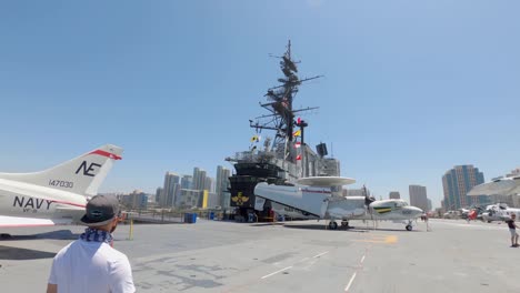 Tourists-walking-on-flight-deck-of-the-USS-Midway-Museum-with-downtown-cityscape-in-background