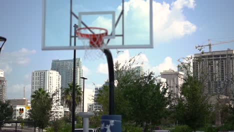 Downtown-cityscape-business-district-skyscrapers-in-the-distance-panning-across-bokeh-basketball-court-hoop-foreground