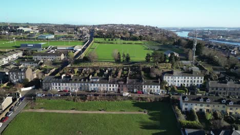 Green-in-the-city-of-Cork,-Ireland-an-aerial-view-over-sport-centre,-pitch-and-putt-and-public-green-area-with-river-Lee-and-row-of-houses