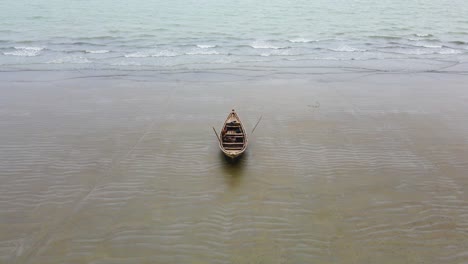 Aerial-tilt-shot-of-a-lone-wooden-boat-on-calm-sea-beach-of-Bangladesh
