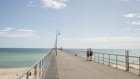 Time-lapse-of-tourists-walking-along-Glenelg-Jetty-at-midday,-zoom-in