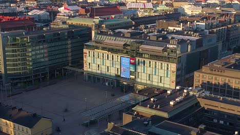 Aerial,-zoom-in-view-of-the-Kamppi-shopping-mall,-sunny,-summer-morning-sunrise,-in-Helsinki,-Finland--,-tracking,-drone-shot
