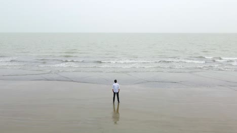 Man-standing-on-the-seashore-back-on-camera-looking-at-the-vast-Indian-ocean-wearing-white-long-sleeves-and-jeans-hands-in-pocket