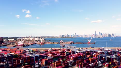 Industrial-vehicles-moving-and-sorting-shipping-containers-at-busy-shipping-port-near-New-York-City---moving-side-pan-angle-aerial-footage