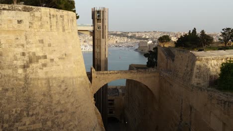 Upper-Barrakka-Lift-Arriving-From-The-Harbour,-With-The-View-Of-Birgu-And-Isla-In-The-Background