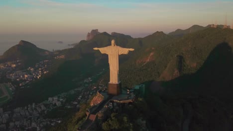 Drohne-Fliegt-Während-Der-Goldenen-Stunde-Rückwärts-Von-Cristo-Redentor-Mit-Der-Stadt-Rio-In-Der-Ferne