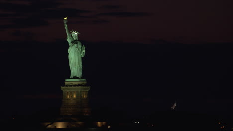 Estatua-De-La-Libertad-De-Noche-Con-Las-Luces-Encendidas,-Enmarcada-A-La-Izquierda