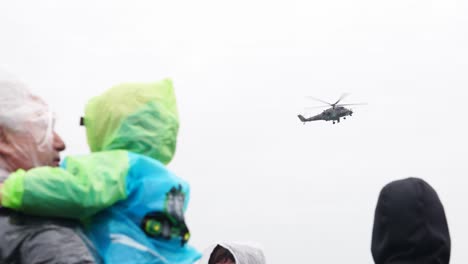 Un-Hombre-Sostiene-A-Un-Niño-Pequeño-Mientras-Un-Helicóptero-De-Ataque-Militar-Flota-Durante-Una-Exhibición-Aérea