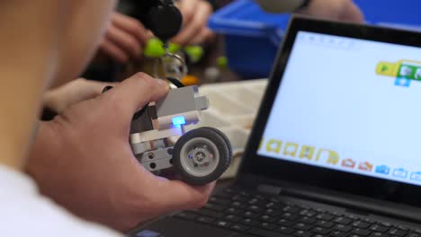 An-anonymous-student-rotating-and-handling-a-robotic-car-in-front-of-a-computer-screen-in-a-programming-lesson