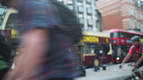 Cyclists-passing-by-in-frame-in-London-with-traditional-red-busses-in-background,-blurred-scene