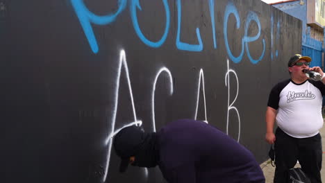 Black-Lives-Matter-Protest,-Los-Angeles,-USA,-Mann-Mit-Schwarzer-Maske-Schreibt-Ein-Taxi-An-Die-Wand-Gegen-Polizei-Und-Polizisten,-Zeitlupe