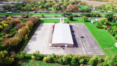 Sideways-aerial-of-a-large-warehouse-and-vacant-lot-amidst-colorful-fall-foliage
