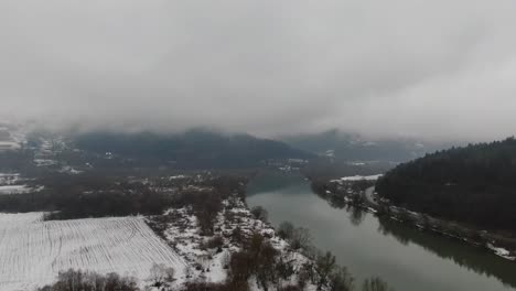 Misterioso-Paisaje-Montañoso-Con-Río-Y-Cielo-Nublado-En-La-Nieve-Invernal,-Panorama-Aéreo