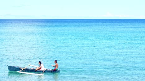 Two-youg-filipino-children---teens-paddle-past-in-a-canoe-on-a-bright-sunny-day