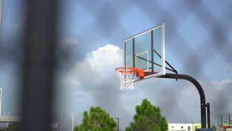 Unfocused-playground-fencing-observing-basketball-hoop-against-cloudy-blue-sky