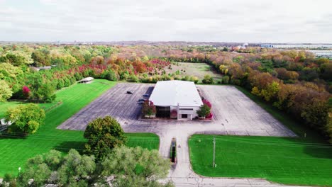 A-drone-view-of-a-large-warehouse-and-vacant-lot-amidst-colorful-fall-foliage