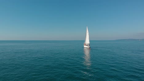 Aerial,-drone-shot-towards-a-white-sailboat,-full-of-people,-sailing-on-the-black-sea,-sunny-day,-in-Adjara,-Georgia