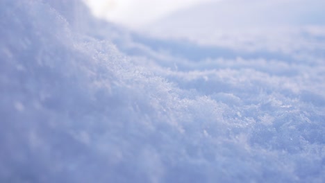 4K-close-up-footage,-capturing-fresh-powder-snow-falling-on-top-a-snow-mound,-in-an-icy-cold-winter-landscape-setting