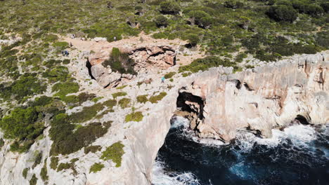 Drohnenaufnahme,-Die-Nach-Rechts-Fliegt-Und-Einen-Meeresbogen-Mit-Touristen-Einfängt,-Die-In-Der-Nähe-Von-Cala-Varques-Auf-Mallorca-Herumlaufen