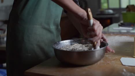 Fully-raised-dough-mix-plucked-out-of-steel-bowl-using-baking-spoon,-filmed-as-medium-close-up-slow-motion-shot
