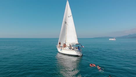 White-sailboat,-full-of-people,-sailing-on-the-black-sea,-bright,-sunny-day,-in-Adjara,-Georgia---Aerial,-drone-shot
