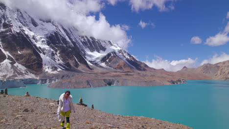 Tilicho-Lake-Manang-Nepal,-female-tourist-treks-World's-Highest-Altitude-Lake,-Annapurna-Mountain-landscape-drone-shot,-clouds,-snows,-nature,-sunny-weather,-blue-lake-4K