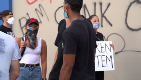Junge-Frau-Mit-Maske-Und-Kaputtem-Systemschild-Bei-Black-Lives-Matter-Protest-In-Kalifornien,-USA